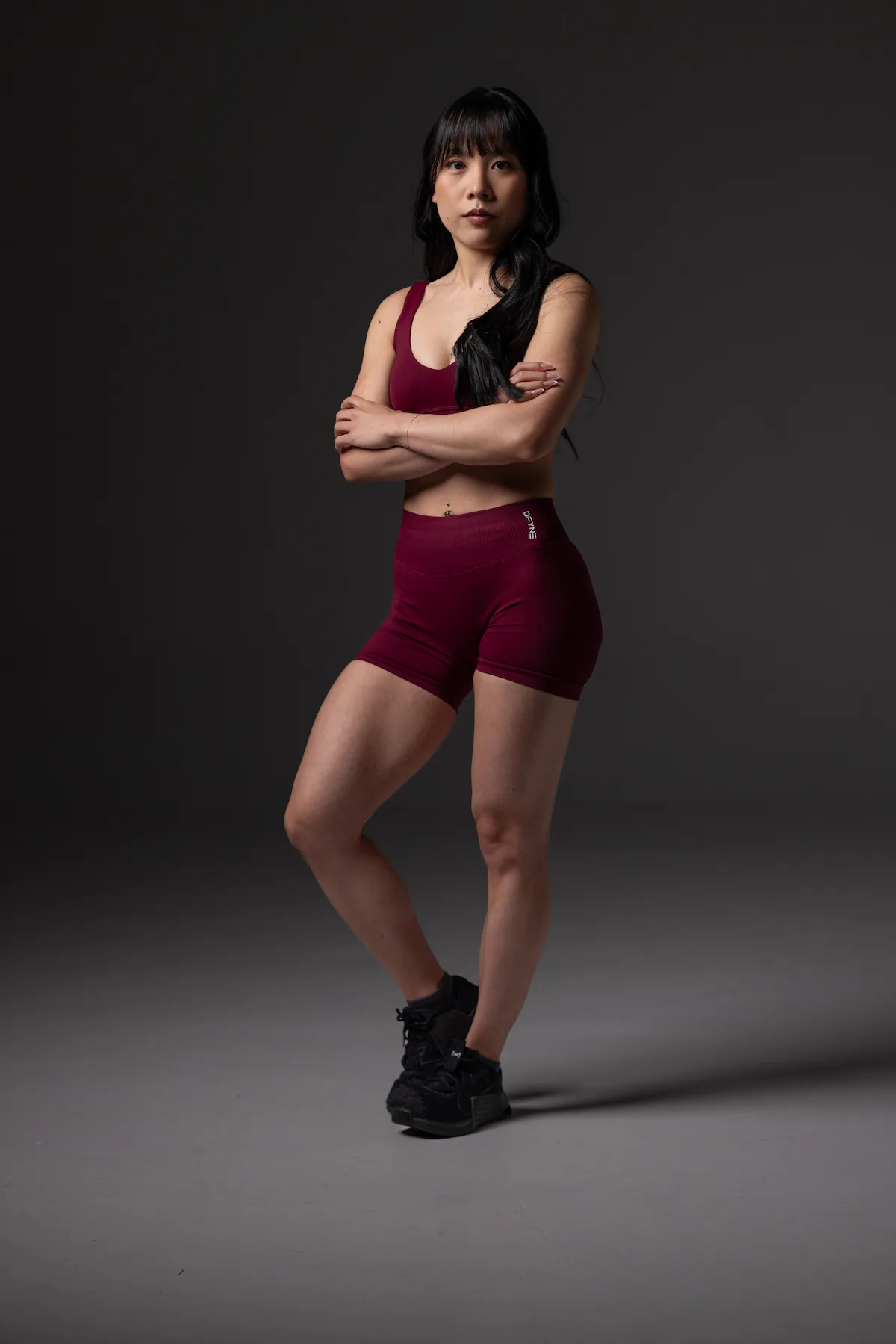 Kaia in a maroon workout outfit posing with her arms crossed
