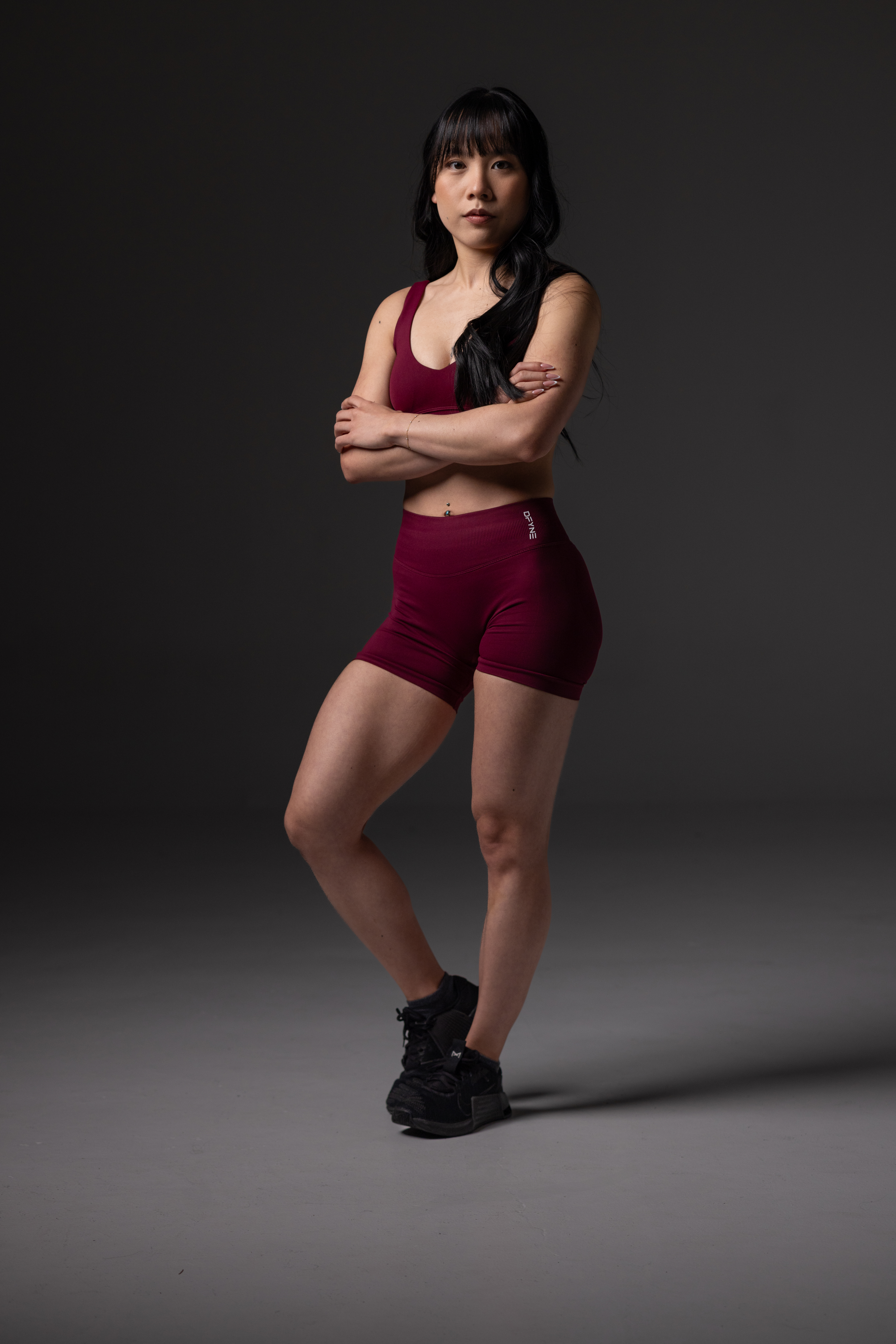 Kaia in a maroon workout outfit posing with her arms crossed